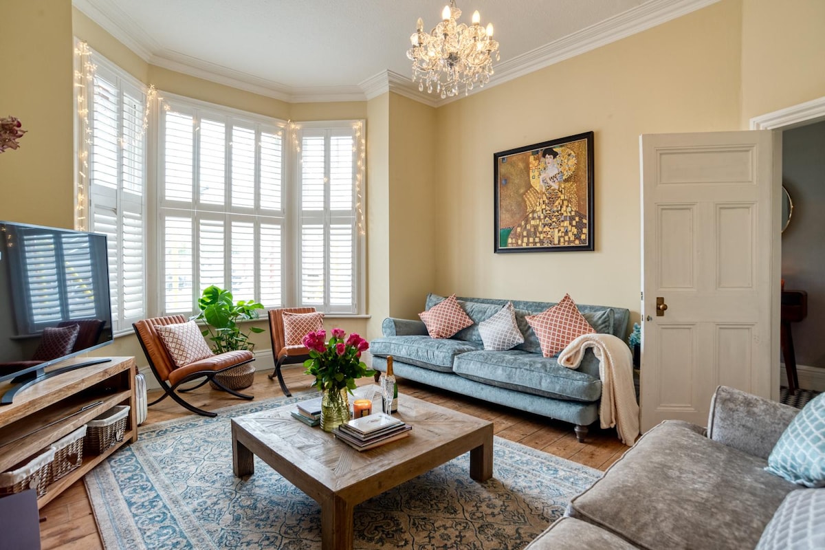 Sunlit living room at Cromer Beach House with a bay window, fireplace and soft blue seating