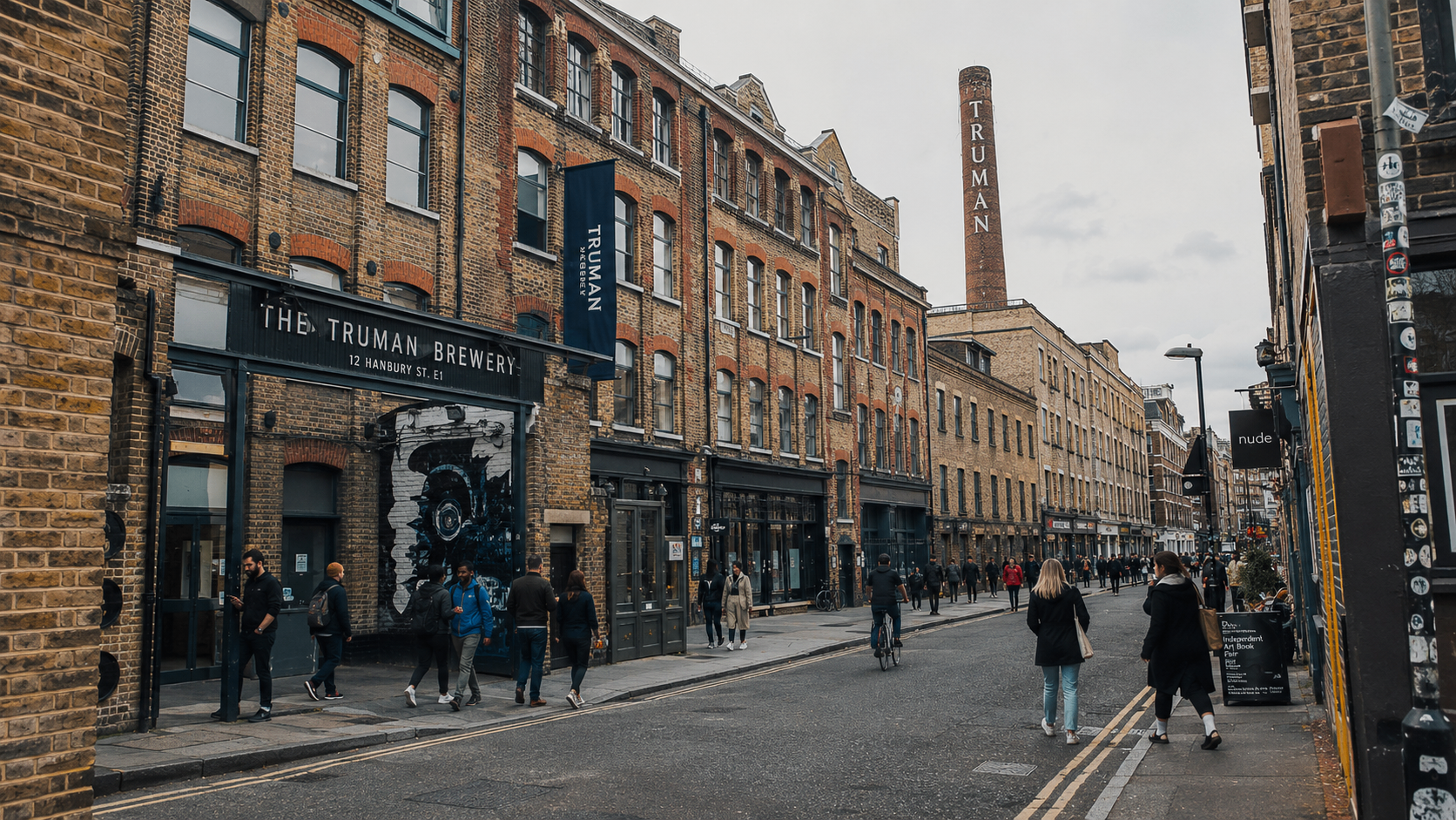 Brick Lane in Shoreditch with the Truman Brewery chimney, brick warehouse frontages, cafes and people walking, east London.