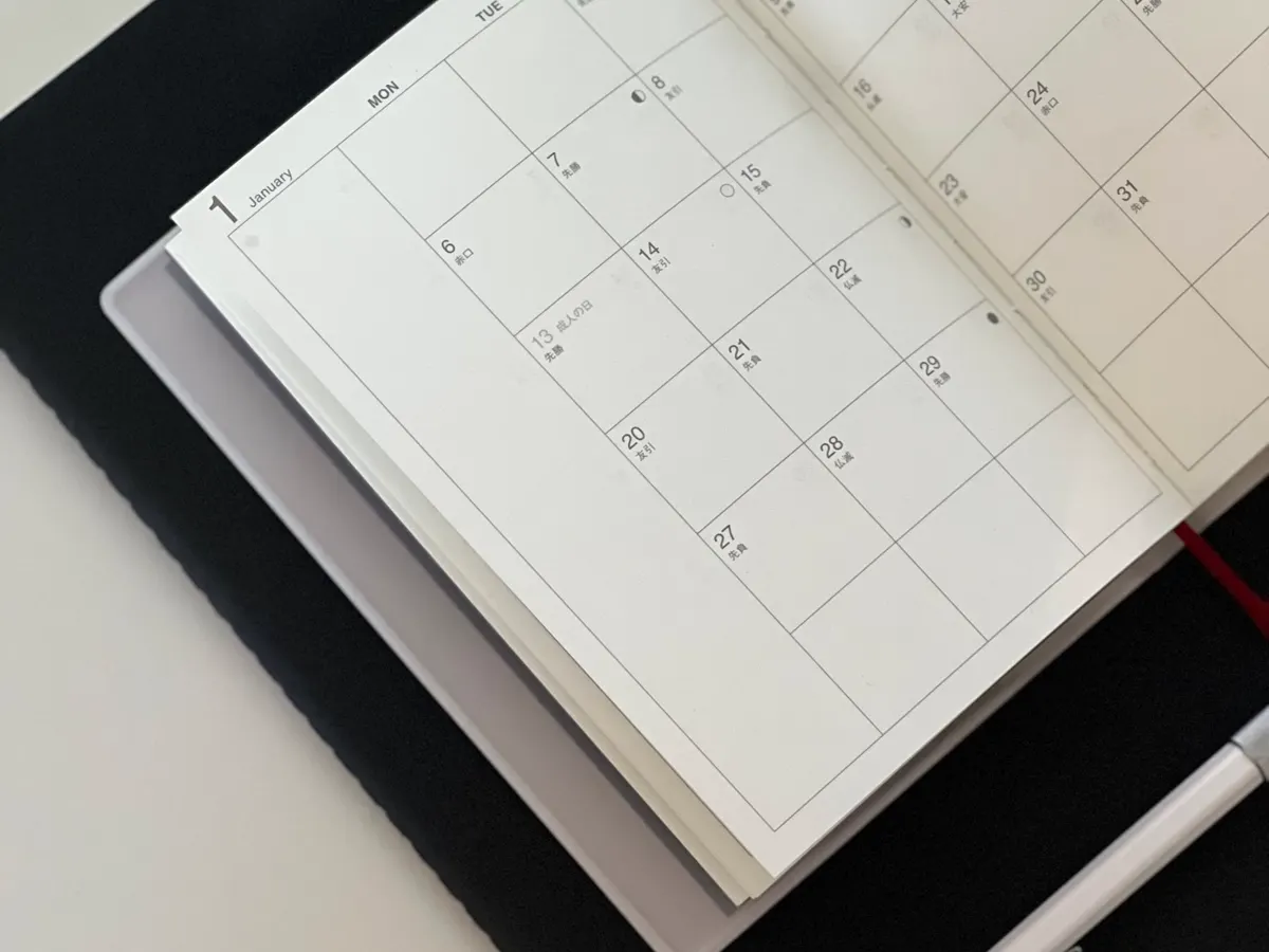 A monthly calendar open on a desk beside a notebook.